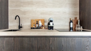 A kitchen with a modern design, featuring a wooden countertop, a coffee maker, and various bottles and glasses.