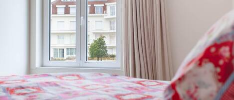 A bedroom with a bed, a window with curtains, and a view of a building outside.
