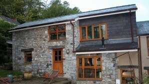 Una casa de piedra con techo inclinado, varias ventanas y un pequeño porche.