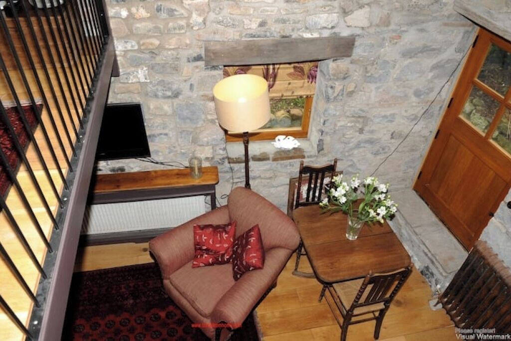 Une pièce chaleureuse avec une cheminée en pierre, une table en bois entourée de chaises, un canapé avec des coussins rouges et un lampadaire.