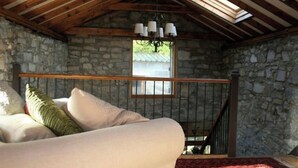 Una habitación acogedora con pared de piedra, techo de madera, un sofá con cojines y una araña.