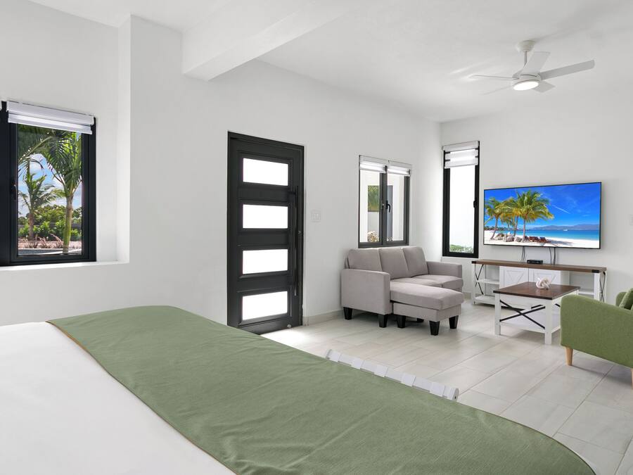 Una habitación de hotel moderna con una cama, una silla verde, un sofá, un escritorio y un televisor.