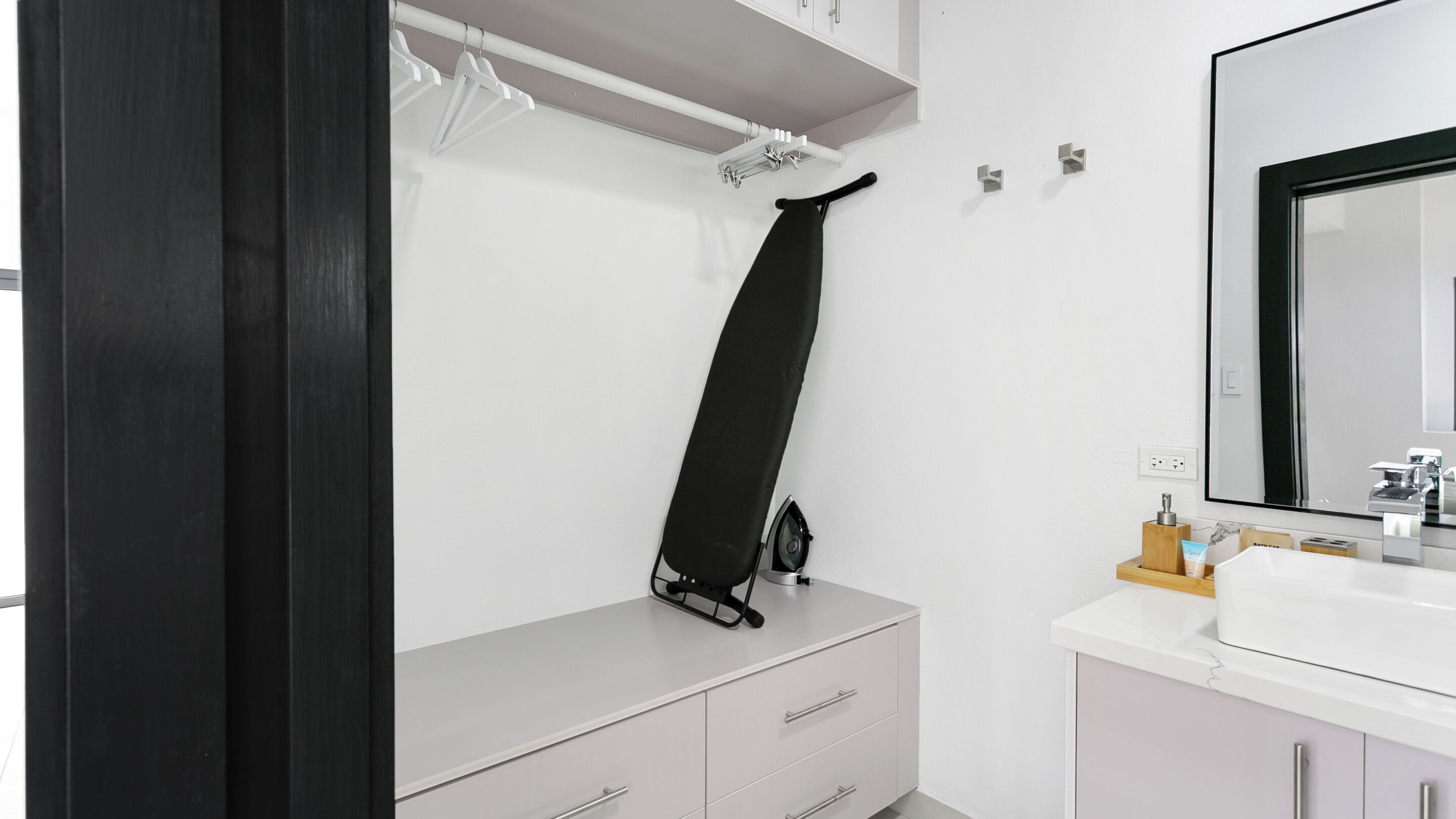 Un baño moderno con un tocador blanco, una estructura de hierro negro y un espejo grande.