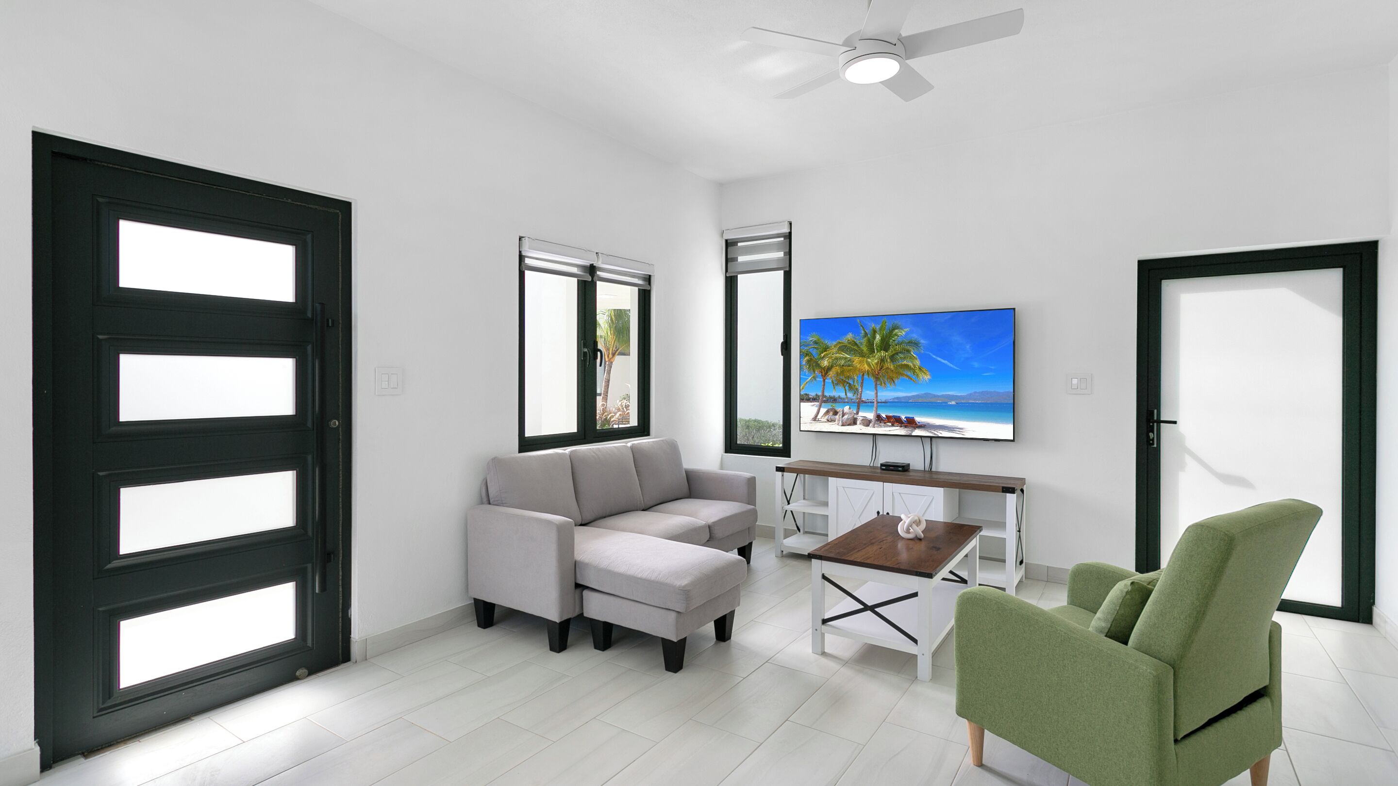 A modern living room with a grey sofa, a green armchair, a coffee table, and a TV displaying a beach scene.