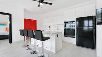 Una cocina moderna con armarios blancos, un refrigerador negro y una puerta roja.