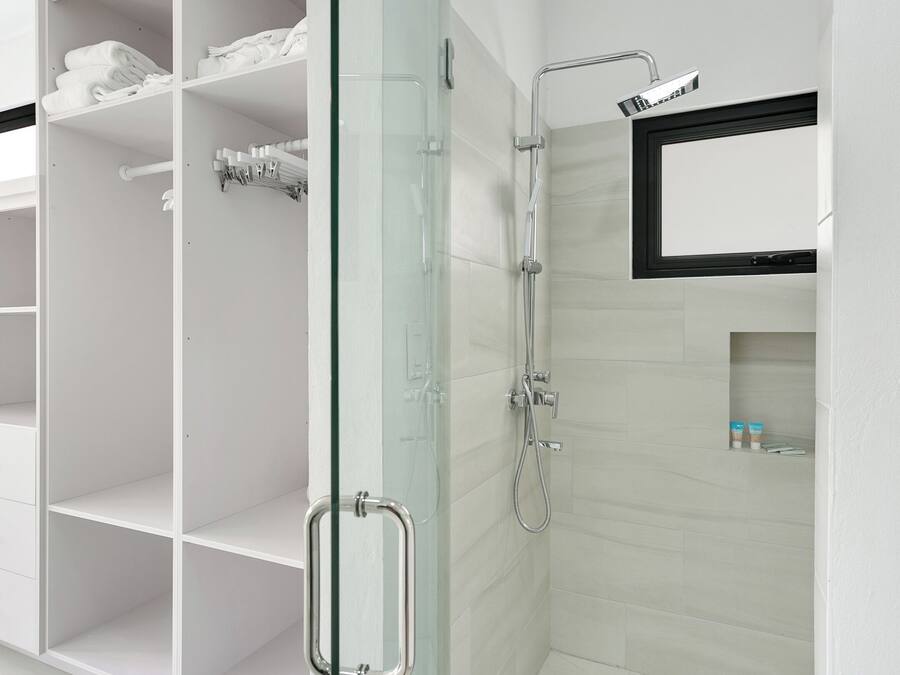 Un baño moderno con cabina de ducha de vidrio, tocador blanco con cajones y una pequeña repisa con artículos de aseo.