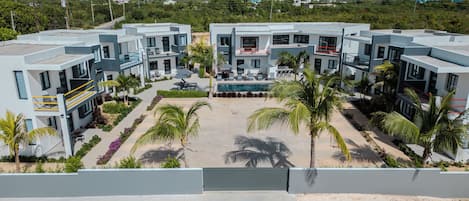 A modern hotel with a central pool, surrounded by palm trees and a landscaped garden.