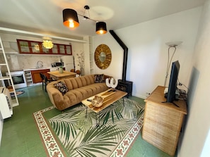 Ein modernes Wohnzimmer mit einer Couch, einem Couchtisch, einem Fernseher und einer Küche im Hintergrund.