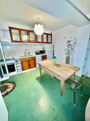 Eine Küche mit Holzausstattung, einer Marmorarbeitsplatte, einem Holzespeise Tisch und einem grün gefliesten Boden.
