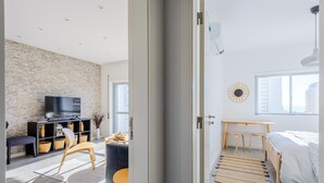 Una sala de estar moderna con pared de ladrillo, un televisor de pantalla plana, una silla de madera, una mesita redonda y un sofá.