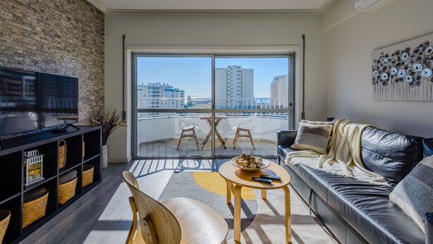 Una sala de estar moderna con un televisor grande, un sofá, una mesa de centro y un balcón con vistas a la ciudad.