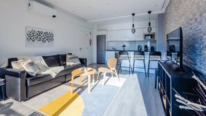 Una sala moderna con sofá, una mesa de centro y sillas, una cocina con comedor, y una pared de acento de ladrillo.