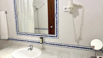 A bathroom with a white sink, a mirror with a decorative frame, a shower, and a toilet paper holder.