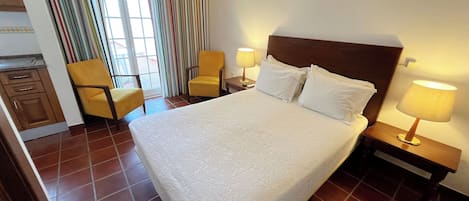 A hotel room with a large bed, two bedside tables with lamps, a chair, a small desk, and a window with curtains.
