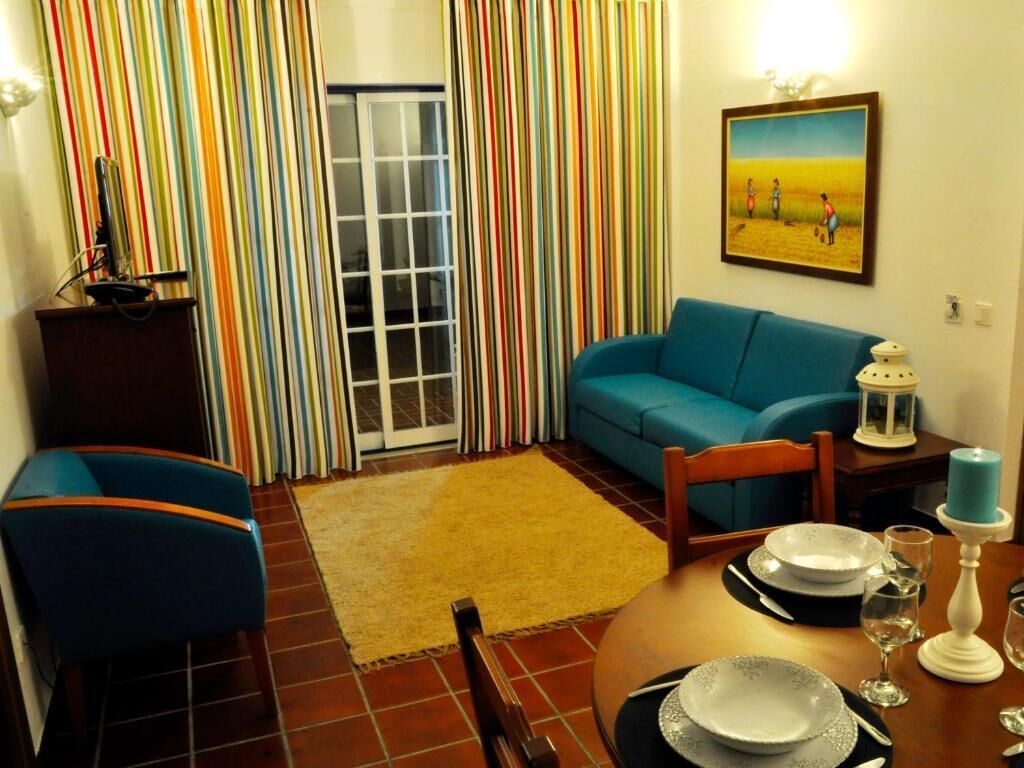 A living room with a blue sofa, a dining table set with plates and glasses, a colorful striped curtain, and a painting on the wall.
