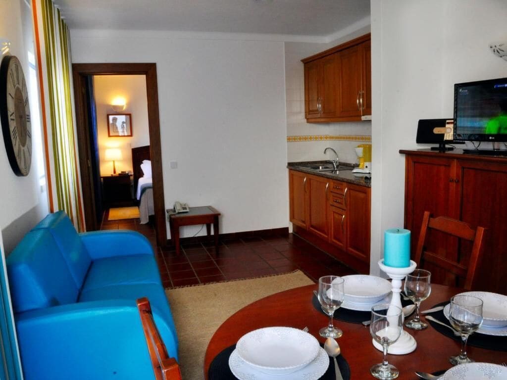 Un comedor con una mesa redonda dispuesta para cuatro personas, un sofá azul, armarios de madera y un televisor al fondo.