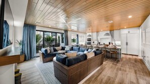 A modern living room with a large sectional sofa, a kitchen area with white cabinets, and a wooden ceiling. - New - Private Beach Access/Zip Line & Waterslide (Sarasota)