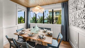 A dining area with a wooden table set for four, large windows with curtains, and a view of palm trees and buildings. - New - Private Beach Access/Zip Line & Waterslide (Sarasota)