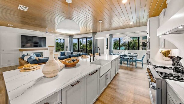 A modern kitchen with a large island, white cabinetry, and a dining area with blue chairs. - New - Private Beach Access/Zip Line & Waterslide (Sarasota)