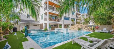 Un hotel de varios pisos con piscina, mobiliario exterior y palmeras.
