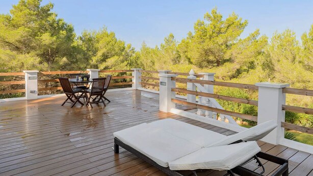 A wooden deck with a table and chairs, a lounge chair, and a white railing. - CASA ES PUIG (Santa Eulalia del Río)