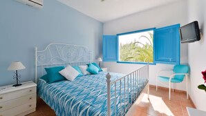 A bedroom with a bed, a nightstand, a TV, a window with blue shutters, and a balcony with a chair. - CASA ES PUIG (Santa Eulalia del Río)