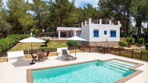 A pool area with a white building, blue shutters, and a wooden fence. - CASA ES PUIG (Santa Eulalia del Río)