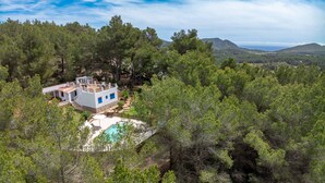 A modern house with a pool surrounded by dense forest, set on a hillside with a view of distant mountains. - CASA ES PUIG (Santa Eulalia del Río)