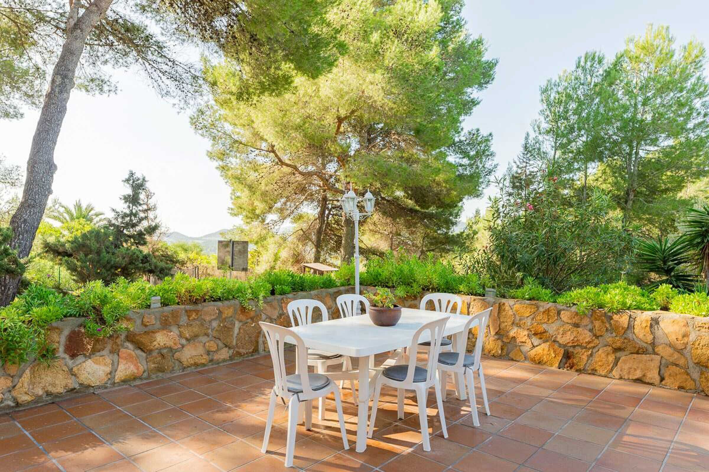 An outdoor patio with a stone wall, white chairs, and a table.