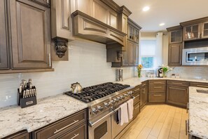 A modern kitchen with dark wood cabinets, a stainless steel stove, and a marble countertop. - Spacious 6BR Beach Home With Elevator Heated Pool - Ideal for Family Vacations (Brigantine)