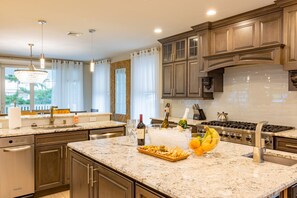 A modern kitchen with granite countertops, stainless steel appliances, and wooden cabinetry. - Spacious 6BR Beach Home With Elevator Heated Pool - Ideal for Family Vacations (Brigantine)
