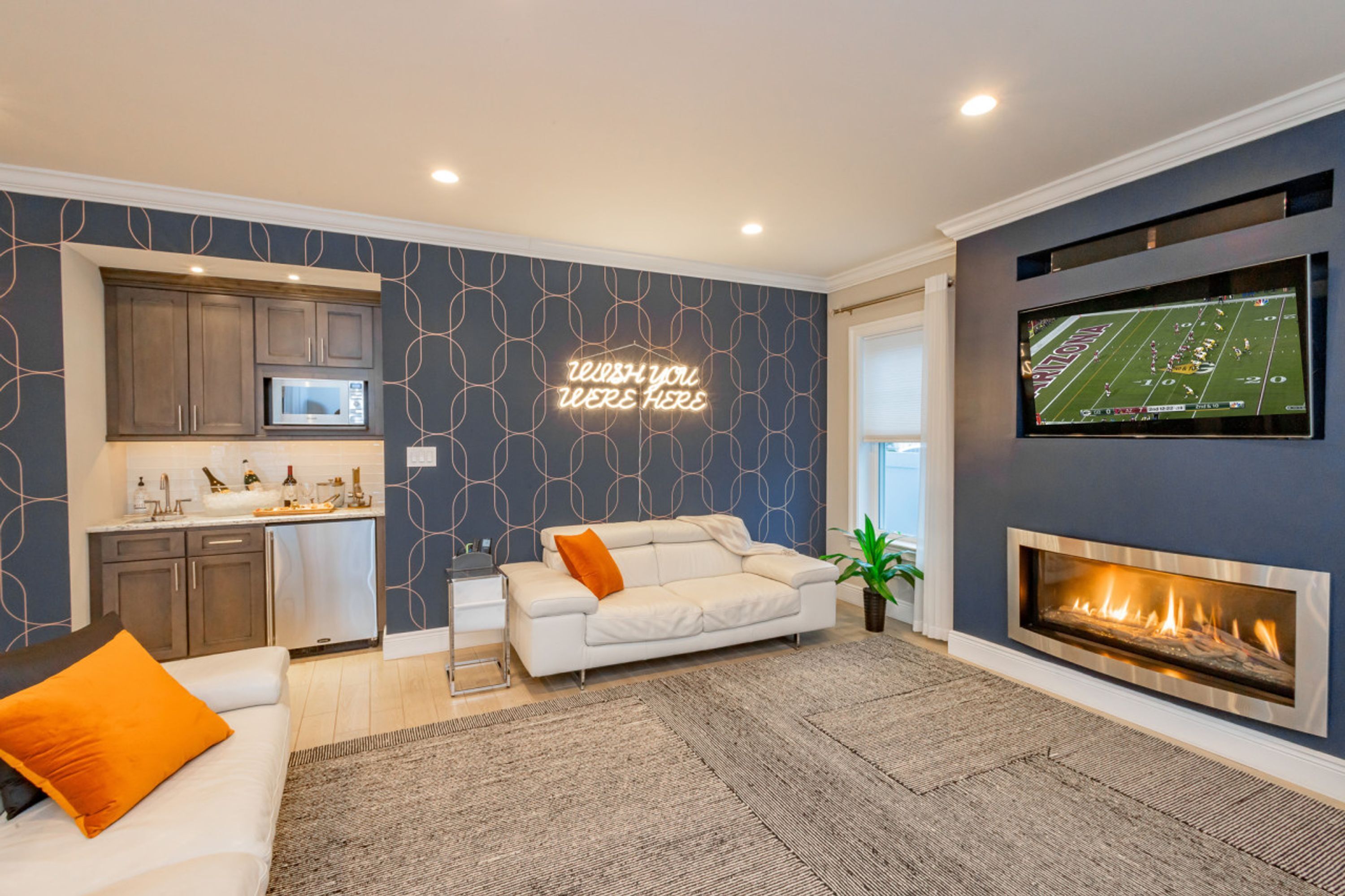A modern living room with a fireplace, a kitchen area, and a neon sign on the wall.