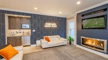 A modern living room with a fireplace, a kitchen area, and a neon sign on the wall.
