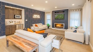 A modern living room with a fireplace, white sofas, a wooden bench, and a kitchen area with a microwave. - Spacious 6BR Beach Home With Elevator Heated Pool - Ideal for Family Vacations (Brigantine)