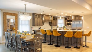 A modern kitchen with a central island, bar stools, and a dining area with chairs. - Spacious 6BR Beach Home With Elevator Heated Pool - Ideal for Family Vacations (Brigantine)