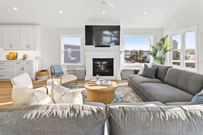 En rummelig stue med pejs, en stor sofa og et tv ophængt over den.