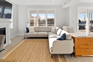 En moderne stue med en beige hjørnesofa, et træsidebord og et stort vindue med udsigt over byen.
