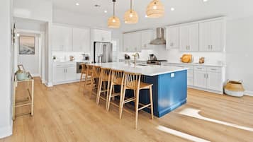 Cocina moderna con armarios blancos, una isla azul, sillas de madera y lámparas colgantes de mimbre.