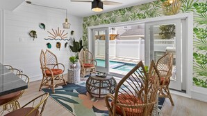 A sunlit room with wicker furniture, a pool view, and a tropical wallpaper. - Heated Pool Hot Tub 5BR Game Room Elevator Cabana (Brigantine)