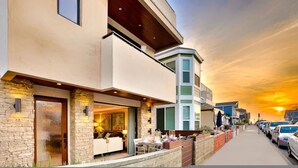 A modern two-story building with a stone facade, a balcony, and a view of parked cars and a sunset.