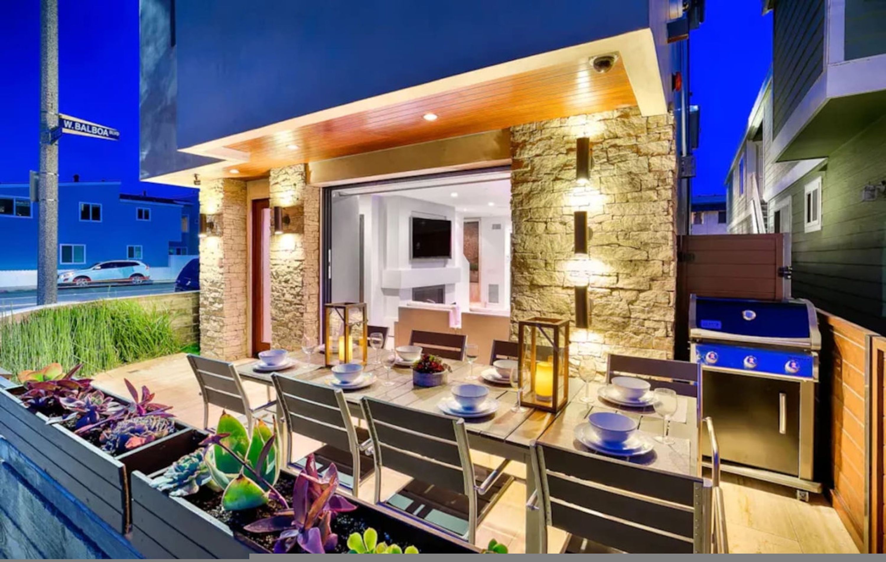 An outdoor dining area with stone walls, a grill, and a view of the street.