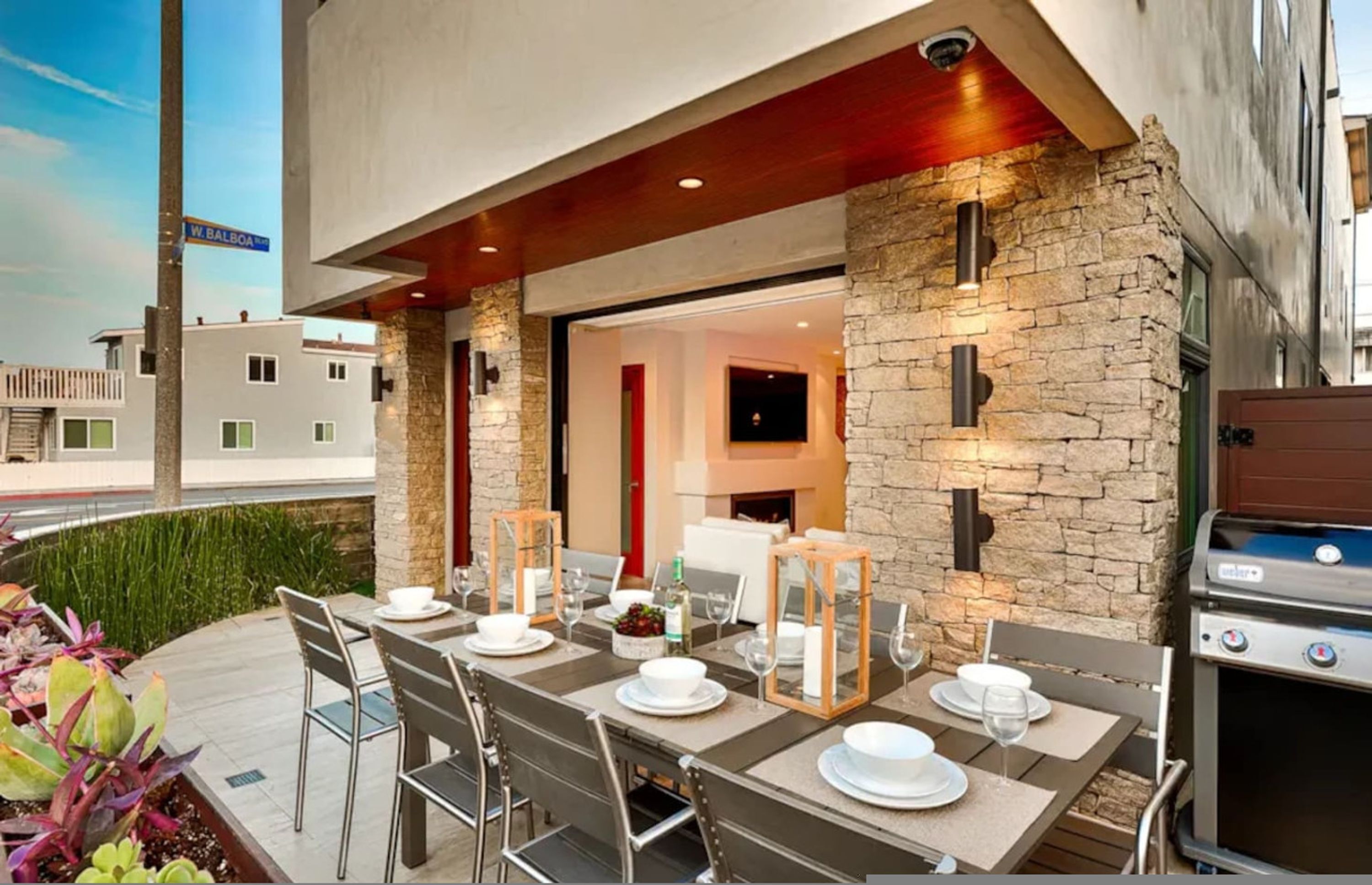 An outdoor dining area with a stone wall, a grill, and a view of the street.