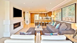 A modern living room with a fireplace, a sofa, a coffee table, and a TV mounted on the wall. - 7 Br 2 Hot Tubs Rooftop Beach Block Ocean View (Newport Beach)