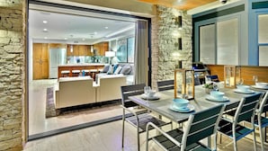 A modern dining area with a stone accent wall, a bar, and a view into the kitchen. - 7 Br 2 Hot Tubs Rooftop Beach Block Ocean View (Newport Beach)