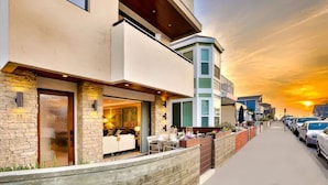 A modern two-story house with a stone facade, a balcony, and a well-lit interior. - 7 Br 2 Hot Tubs Rooftop Beach Block Ocean View (Newport Beach)