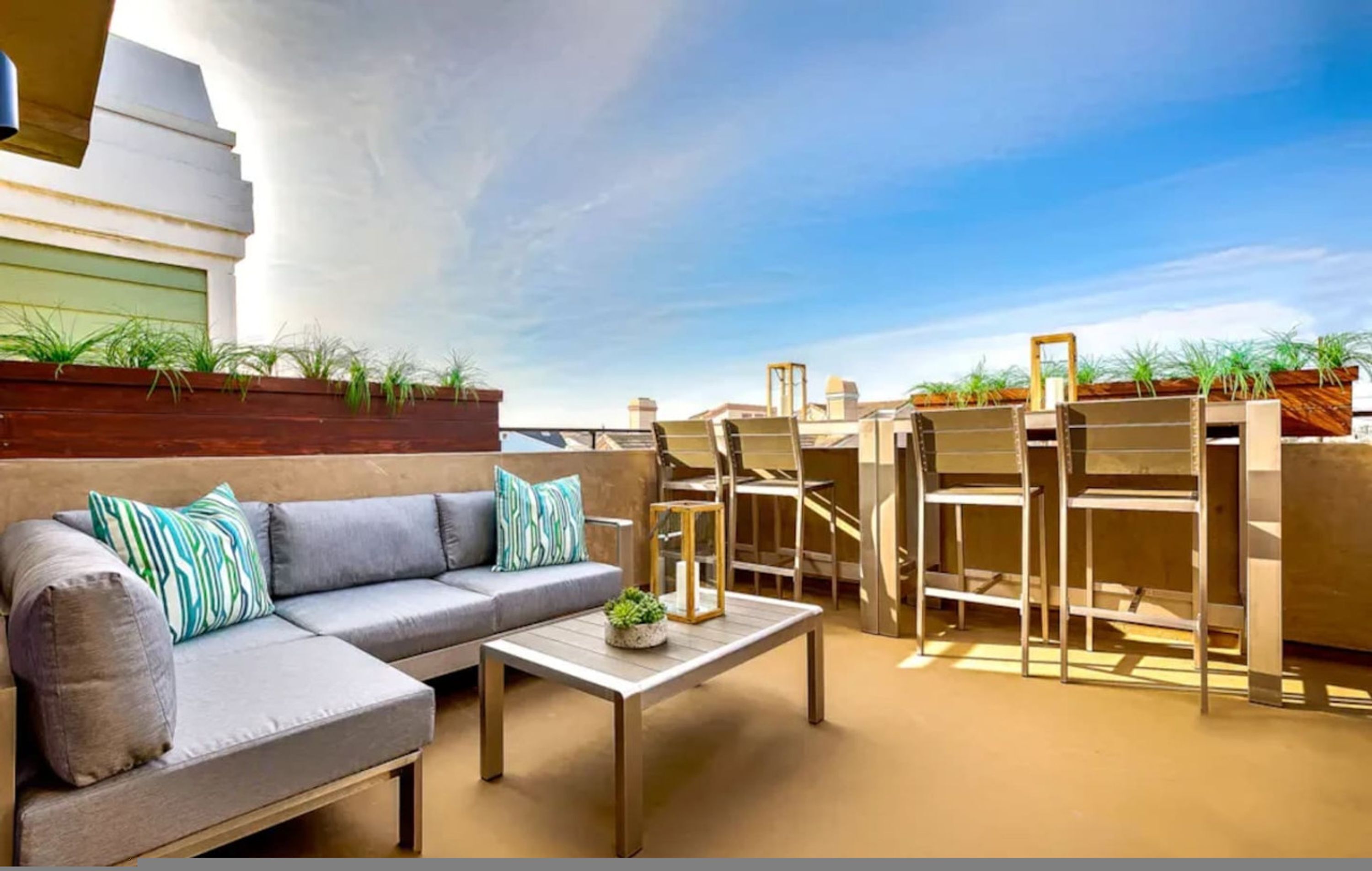 An outdoor seating area with a sofa, coffee table, and chairs, surrounded by planters and a clear sky.