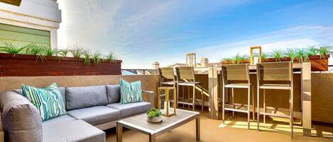 An outdoor seating area with a sofa, coffee table, and chairs, surrounded by planters and a clear sky.