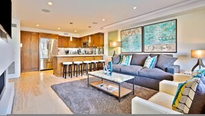 A modern living room with a grey sofa, coffee table, and a kitchen in the background. - 7 Br 2 Hot Tubs Rooftop Beach Block Ocean View (Newport Beach)