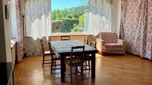 A spacious room with a wooden floor, a dining table with chairs, a sofa, and a large window with curtains.
