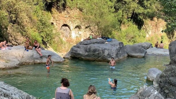 A natural hot spring area with people relaxing and swimming.